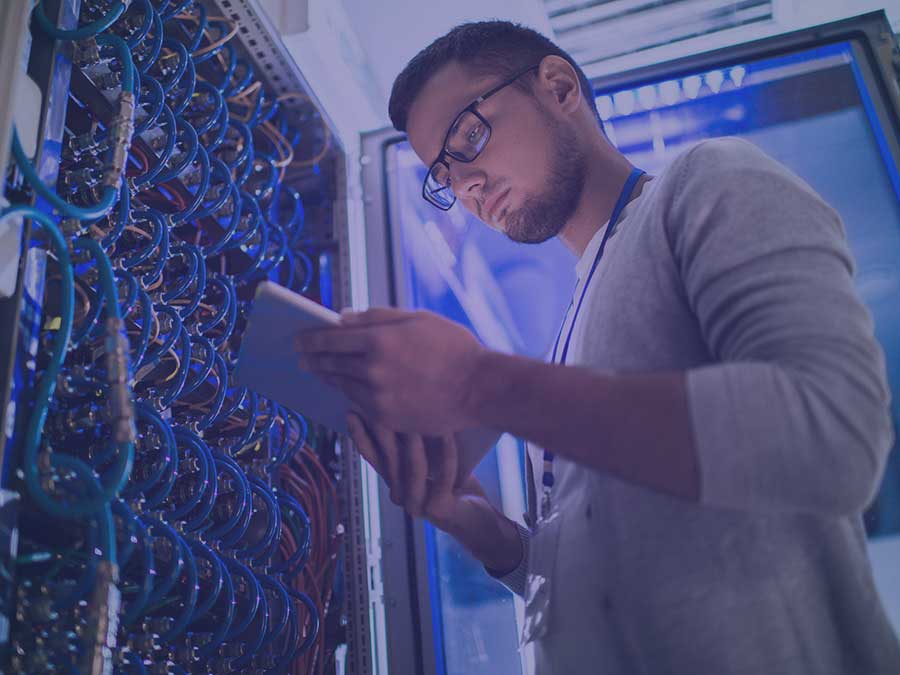 Man using digital tablet standing by server cabinet while working with supercomputer