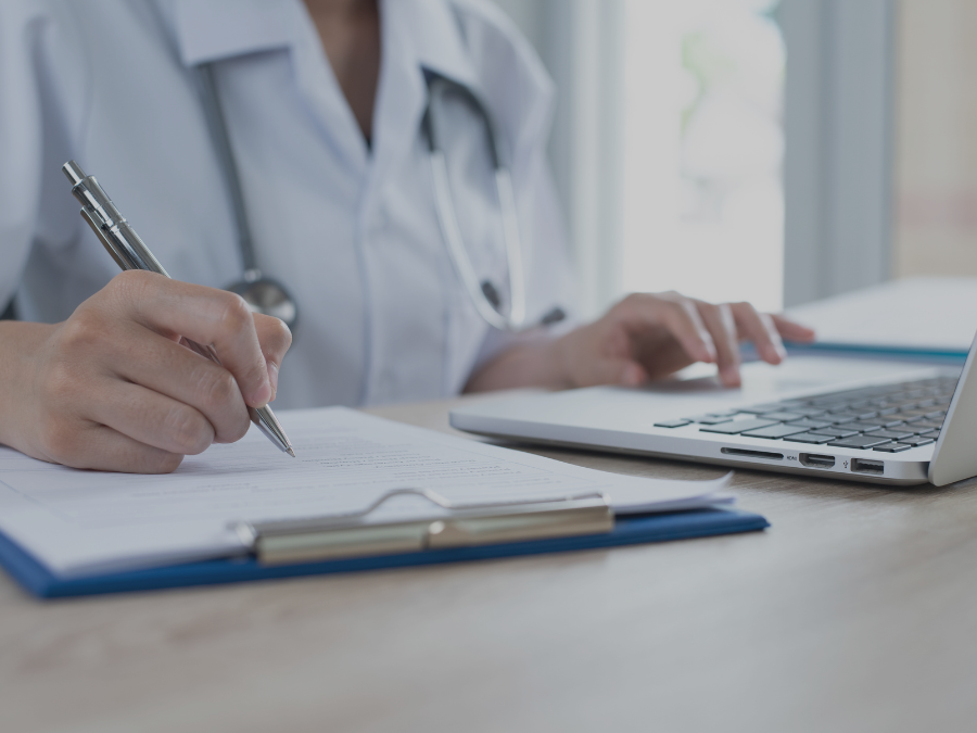 Doctor recording patients information document clipboard and working on laptop computer in medical office